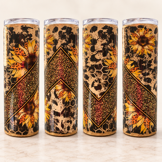 Four tall insulated tumblers with clear lids are lined up on a light marble surface. The tumblers feature a decorative wrap-around pattern combining black leopard spots, honeycomb textures, red speckled diagonal bands, and large yellow sunflower illustrations.