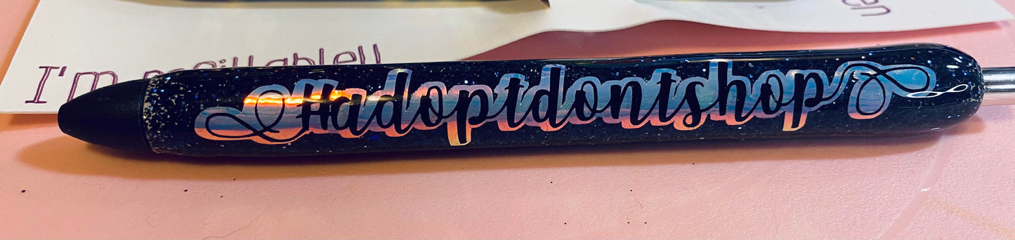 blue glitter coated pen with #adoptdon't shop decal in black on top of a holographic vinyl.