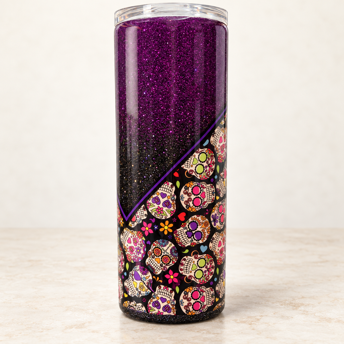 A tall, clear tumbler with a purple glitter upper section and a black lower section decorated with colorful sugar skull patterns, set against a neutral black background.