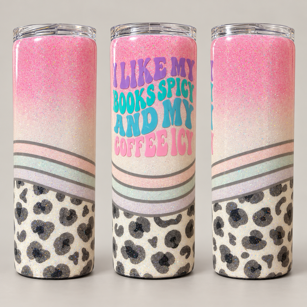 Three views of a glittery insulated tumbler with a pink ombre glitter top, pastel stripes, a black leopard print lower section, and the text 'I LIKE MY BOOKS SPICY AND MY COFFEE ICY' on the front.